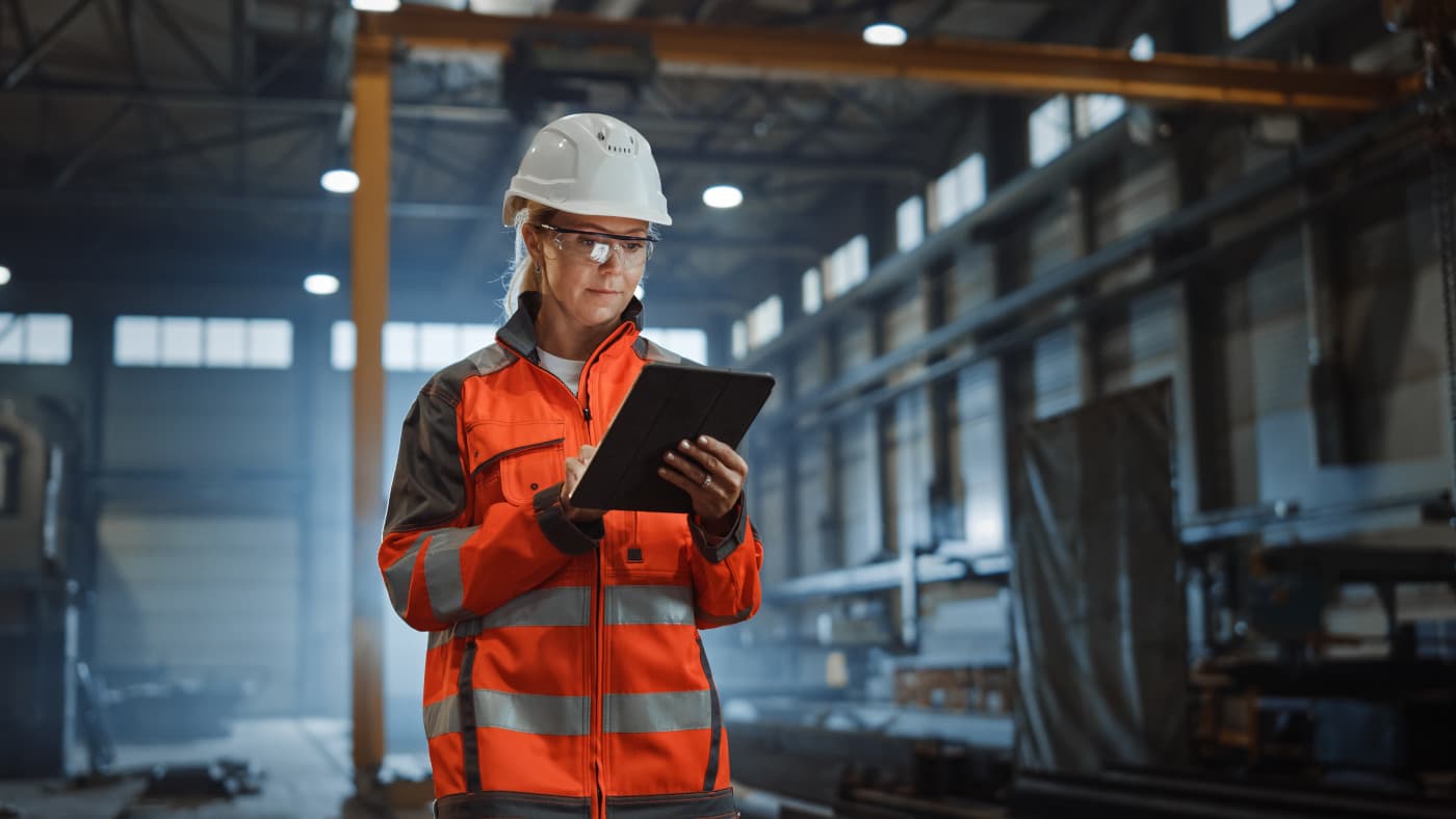 Woman in helmet looking at tablet against the background of a production line.